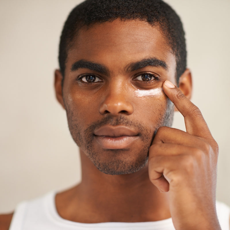 Man applying cream to his face with a neutral background