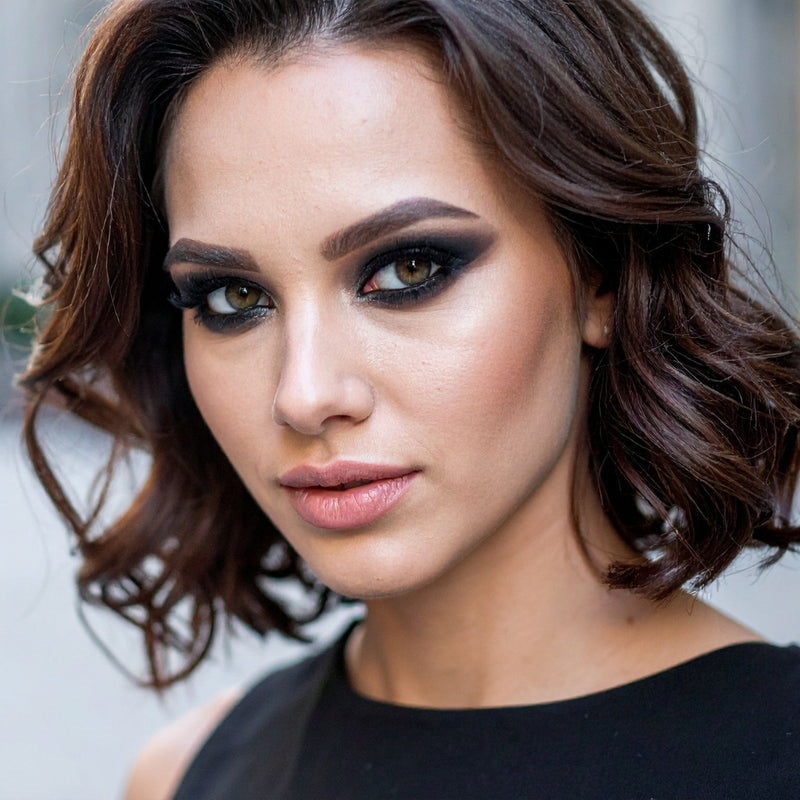 Close-up of a woman with styled hair and makeup against a neutral background