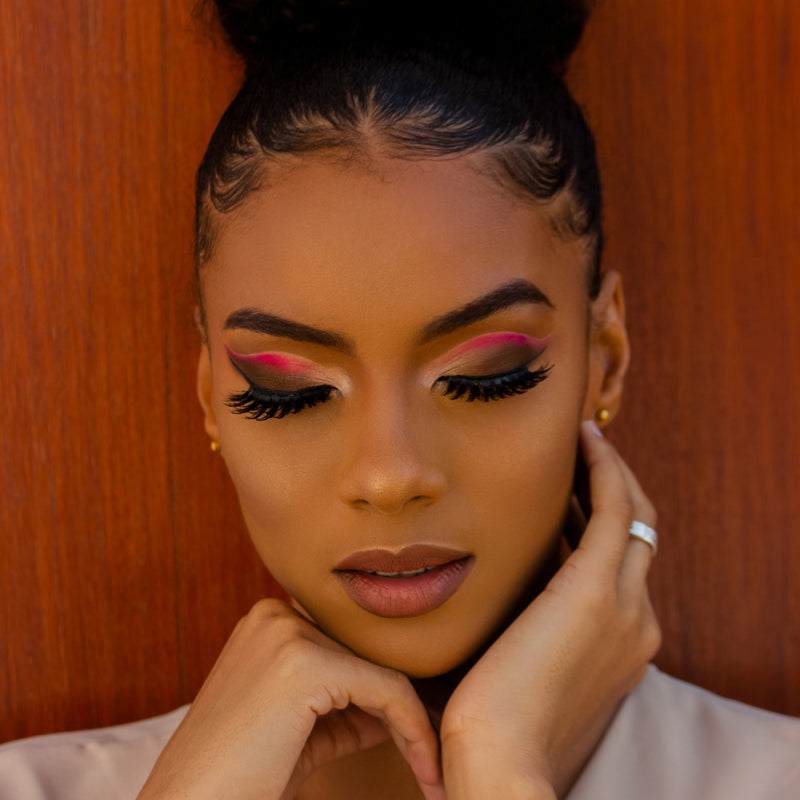 Woman with vibrant makeup and a bun against a wooden background